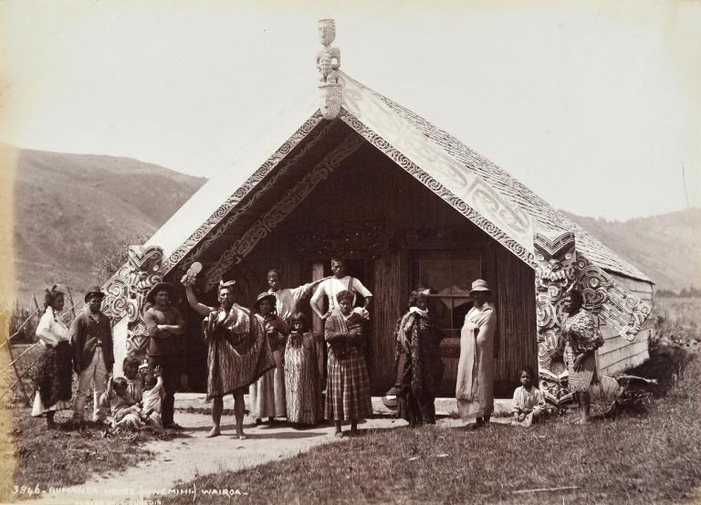 Maori chief and his family in front of a large Meeting House,  Te Wairoa